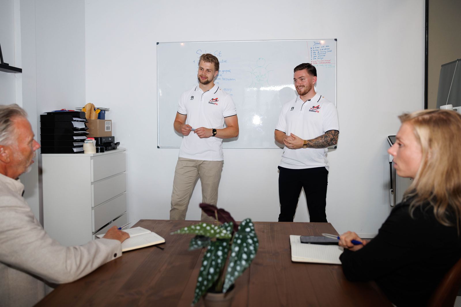 Jan en Wim geven salestraining bij een whiteboard in een vergaderruimte